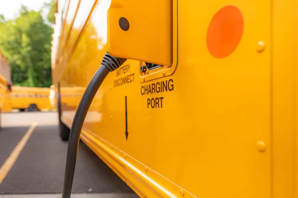 Close-up of open charging port with charging cable plugged in on yellow electric school bus.
